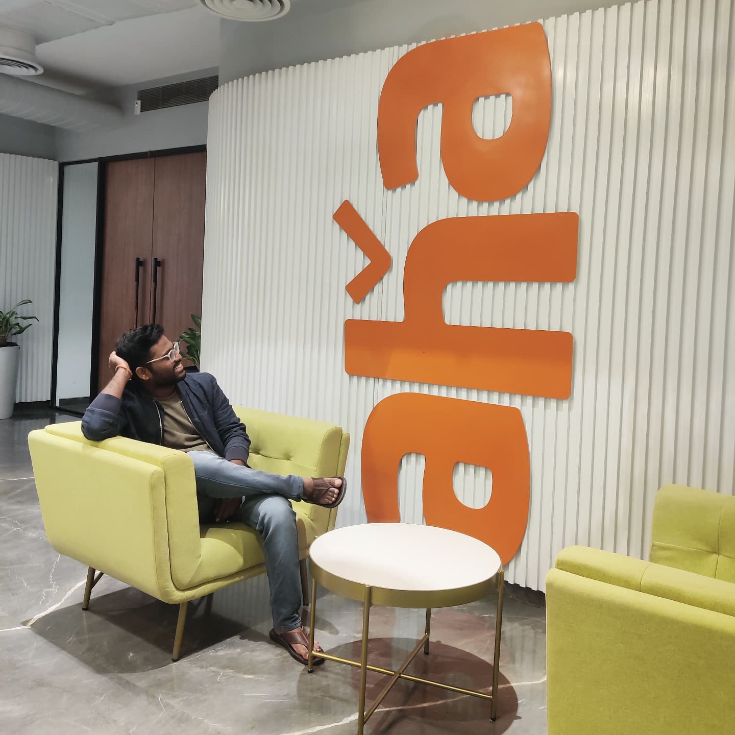 Vamshi at the aha office lounge in front of the aha wall logo